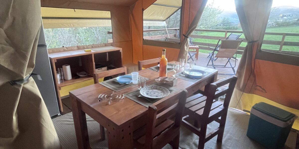 Coin repas à l’intérieur de la tente safari, table en bois et lumière naturelle par l’ouverture
