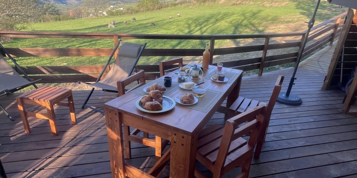 Table et parasol sur la terrasse en bois de l’Aventura Lodge, vue dégagée sur les collines