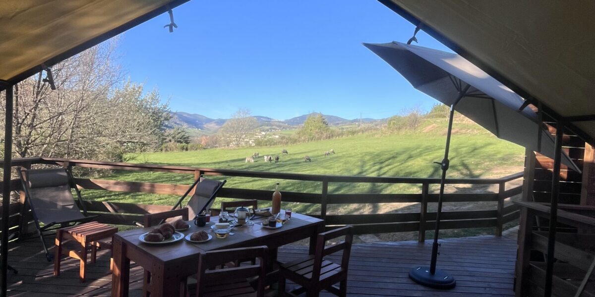 Terrasse en bois de l’Aventura Lodge, table dressée sous la tente safari, ouverte sur la vallée verdoyante